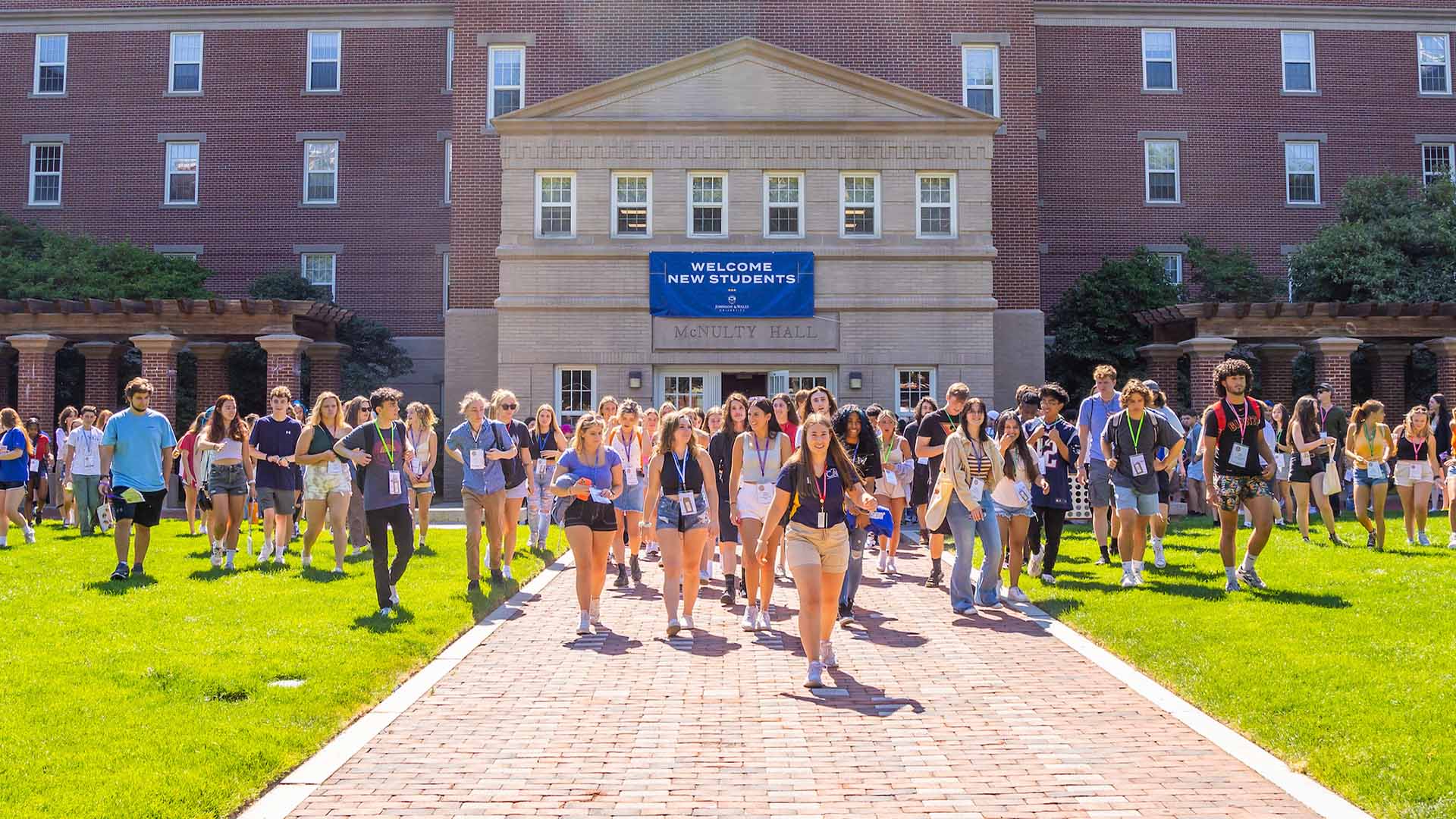 JWU students walking in Gaebe Commons with a sign behind them that reads u0022Welcome New Studentsu0022