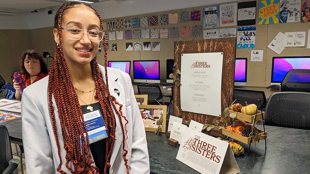 Erika Morais '23 poses with some of the elements her team graphic designed for a culinary students' 