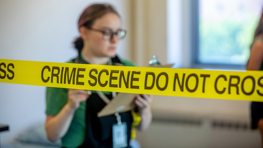 Students investigate a mock crime scene, yellow tape with the words 
